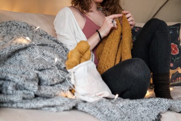 woman sitting on a sofa while knitting a sweater